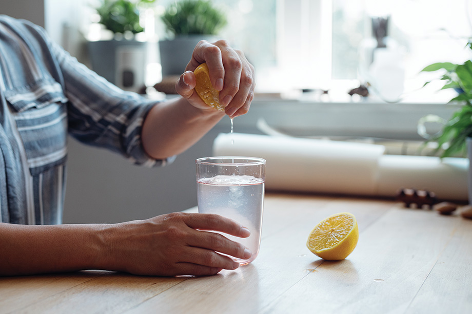 Close up shot of an anonymous young woman's hands squeezing a lemon into a cup of water making lemonade sitting at a wooden table.