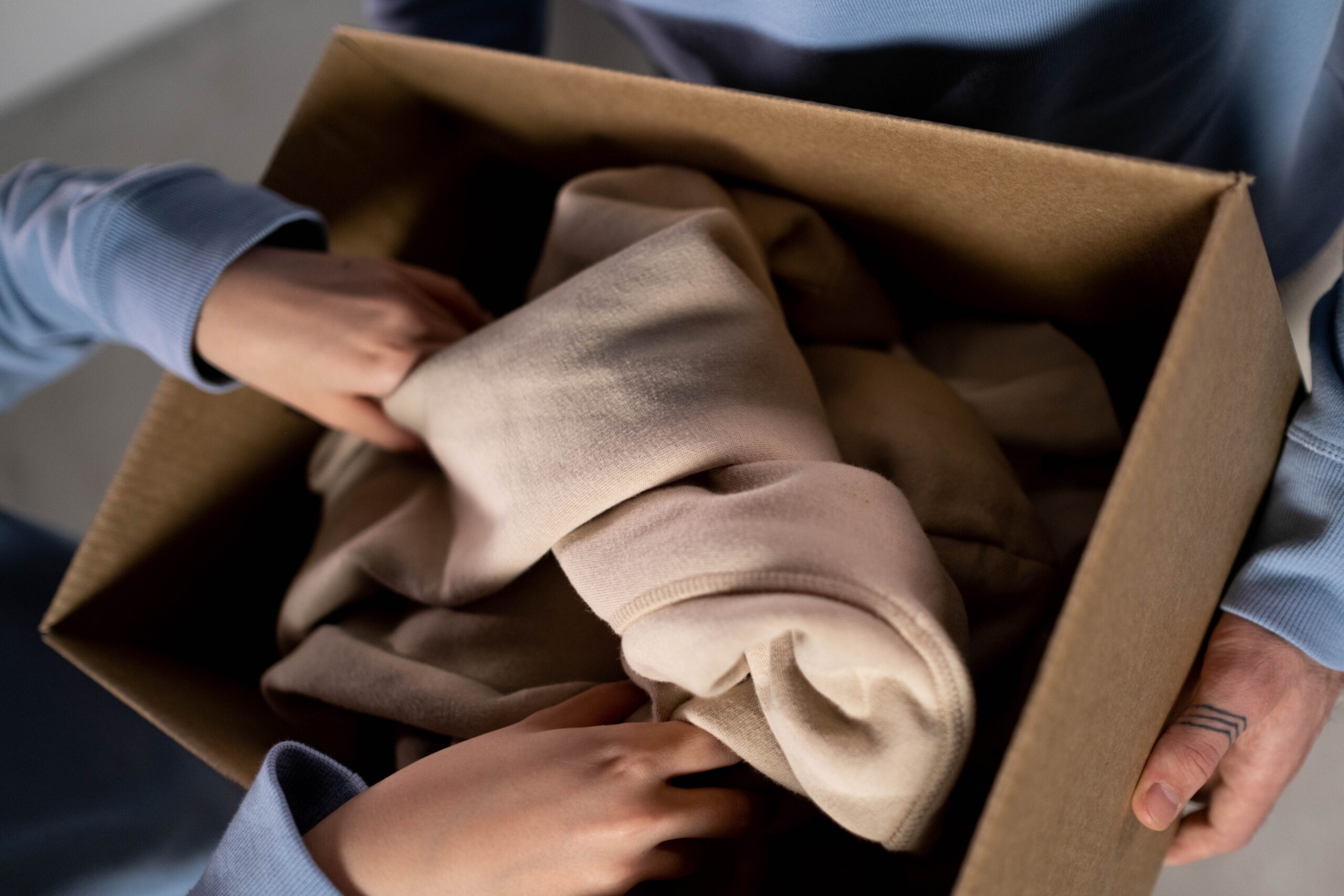 Hands placing clothes into a cardboard box.