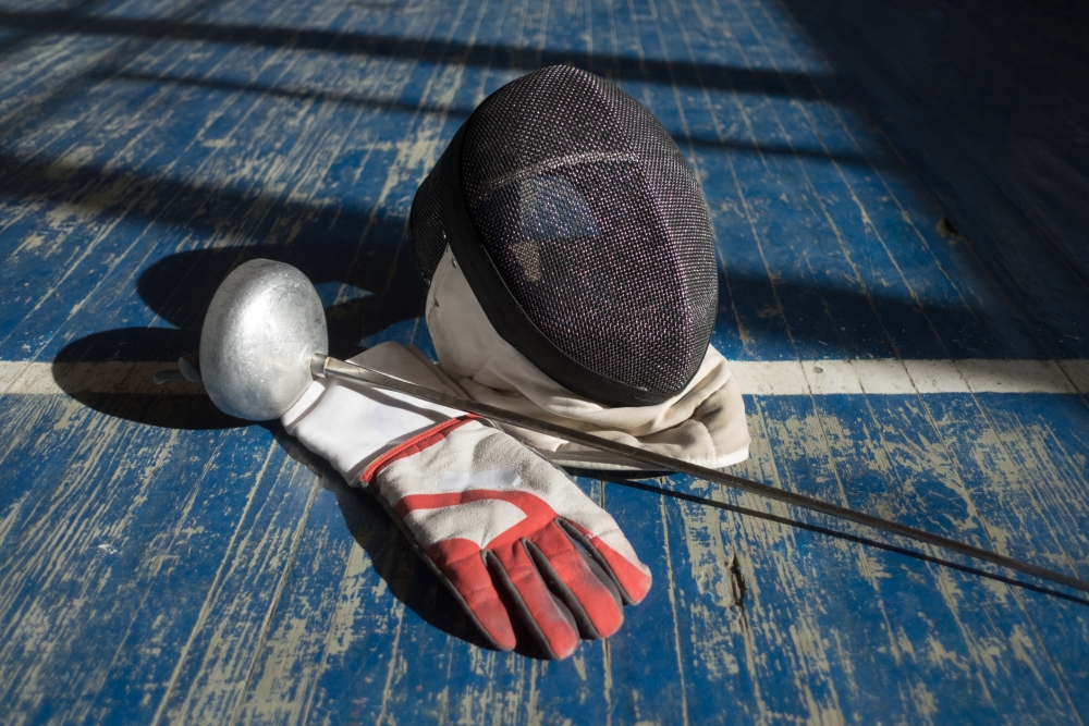 Fencing mask, foil and glove on a blue wood floor.