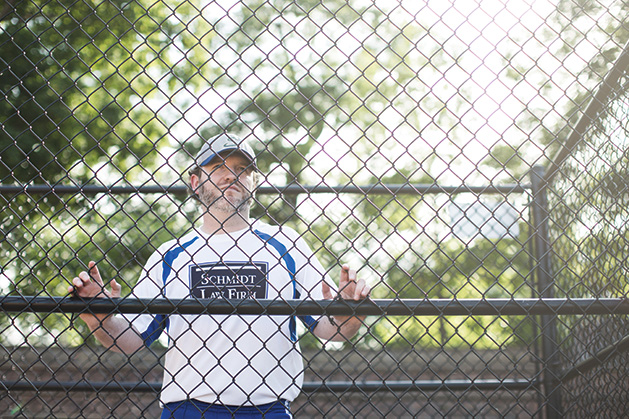 Man behind chain link fence of softball field.