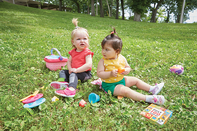 Two babies wearing RubyScootz play on a lawn.
