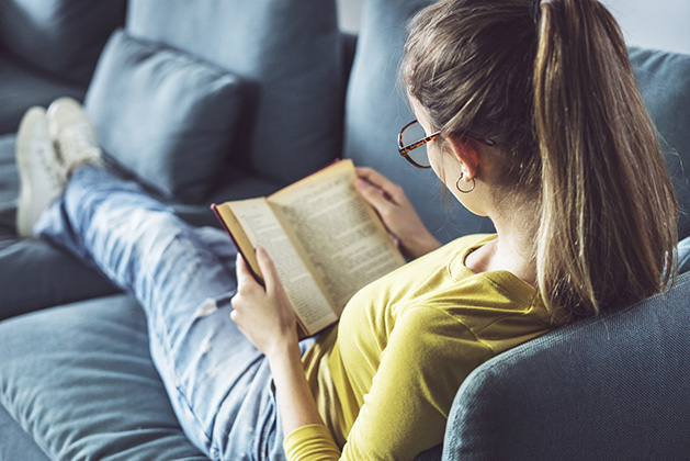 A teenage girl reads a YA novel on her couch.