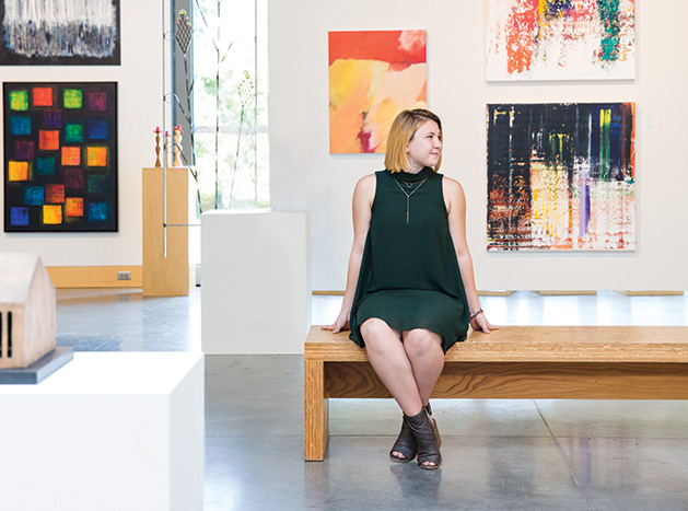 Grace Hanson, part of the 2019 Senior Spotlight, poses in front of a wall of paintings.