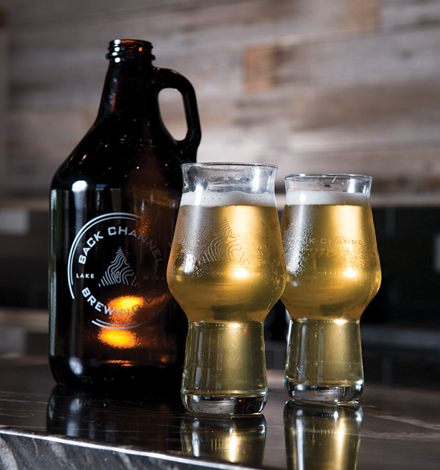 Two glasses of Back Channel Brewing's Soviet Slayer imperial stout stand next to a growler.