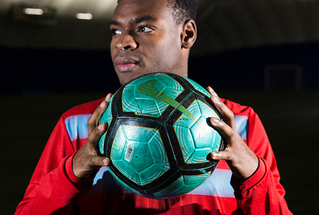 Orono grad Guy Mohs, originally from Haiti, holds a soccer ball.