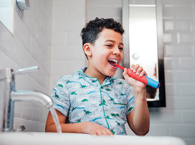 A boy brushes his teeth with an electric toothbrush.