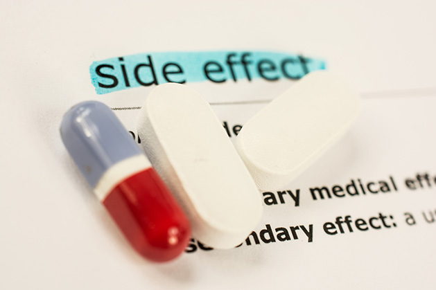 Three pills rest on a piece of paper listing side effects.