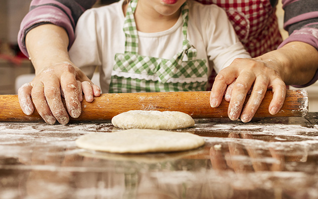 A grandmother helps her granddaughter roll some dough.
