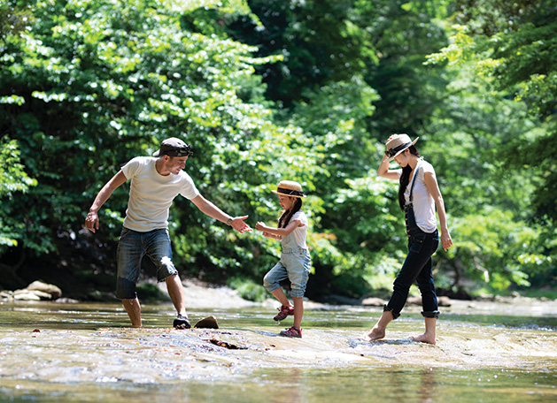 A couple on vacation with their child walks through a river.