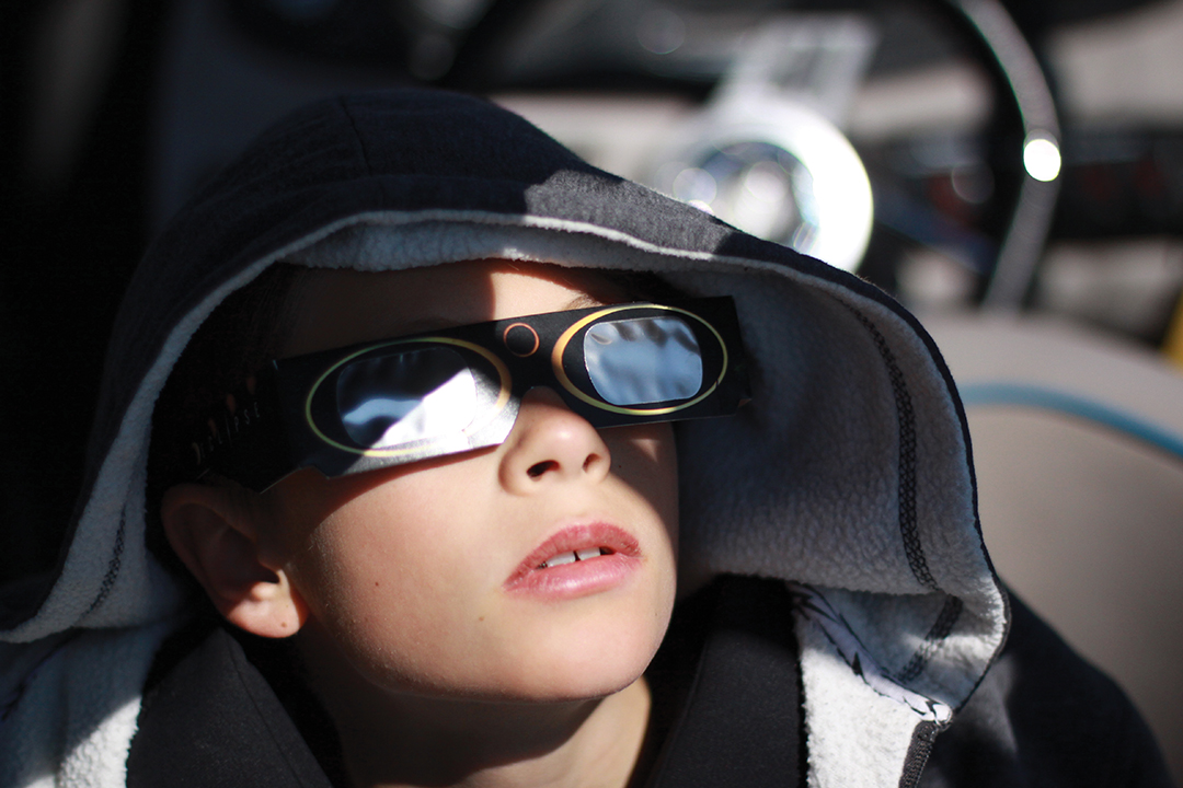 Young boy watching a solar eclipse with protective glasses.
