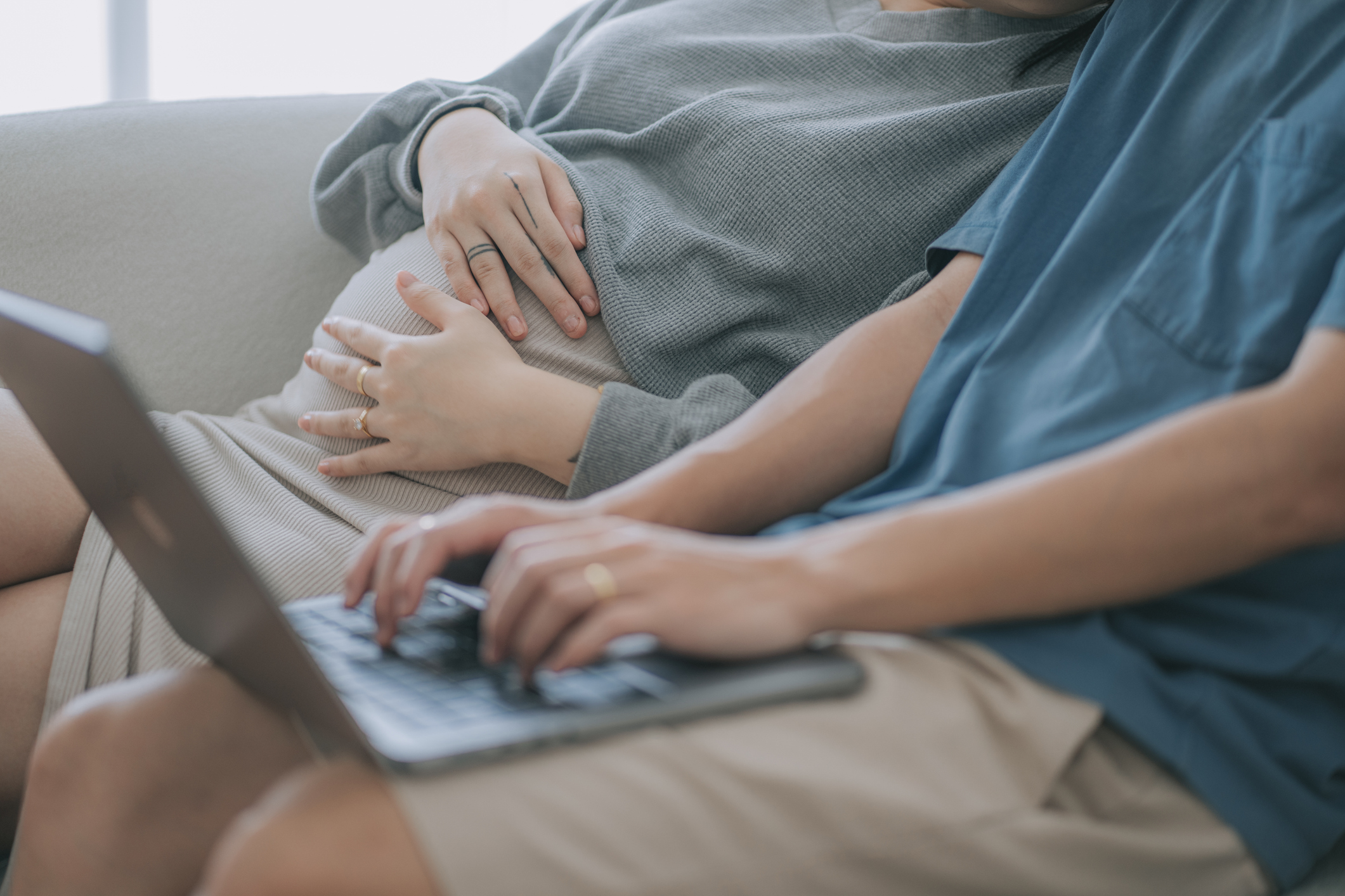 Asian chinese pregnant young woman and husband surfing internet online shopping at home sitting on sofa