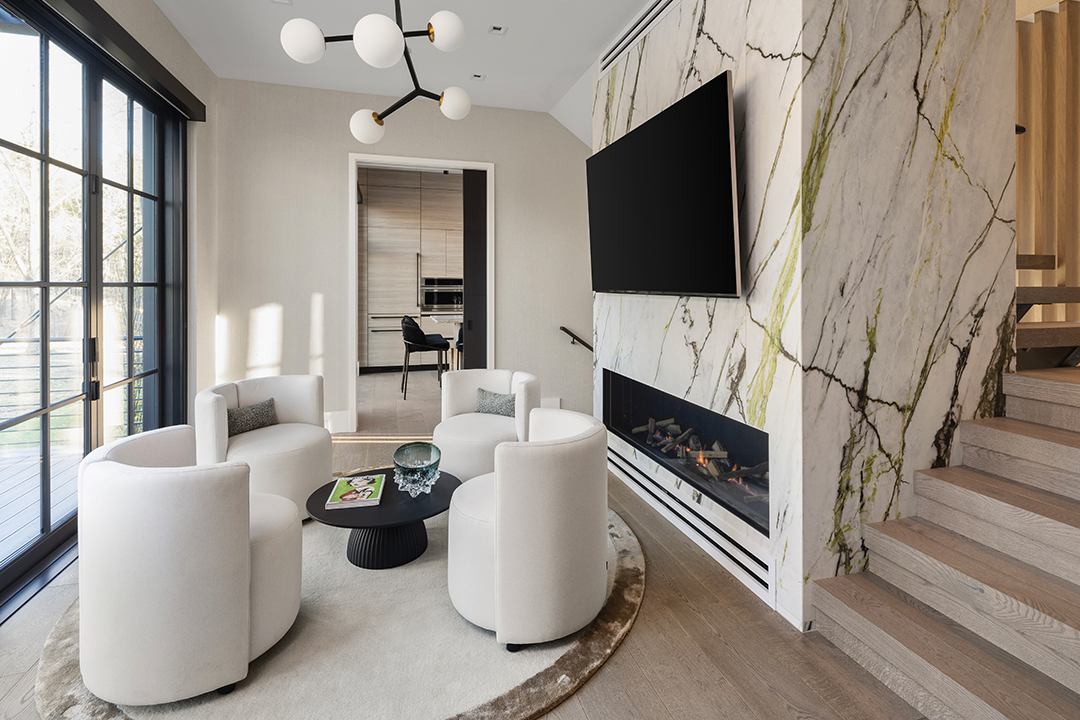 An impressive stone wall on the main level is the “heart” of the guest home, Payares says. It features a long, sleek fireplace on the bottom and a place for a mounted television higher up. “We needed to find a stone that could capture what we were feeling,” she says. “We decided to use one that simulates the growth of tree roots through the shades of lime green and dry green.” Those colors—plus the calm, minimal lines of the curved chairs and rug—lend an organic character to the space. Behind the fireplace is the home’s central staircase, which opens to the foyer and includes wood panels and strip lights, making it another artful composition for guests to enjoy.