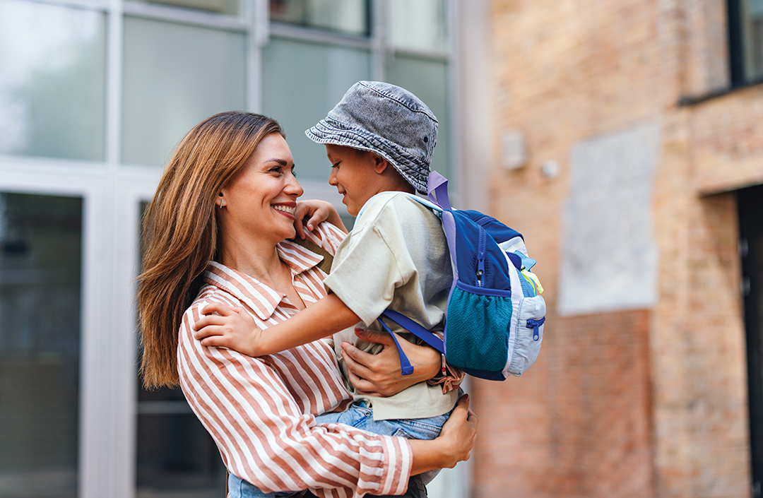 A joyful mother warmly embraces her son as he gets ready for his first day of school, wearing a backpack.