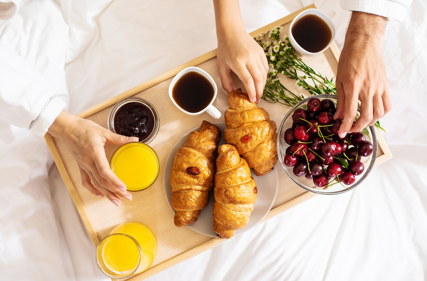 Happy young beautiful family in bathrobes are taking morning breakfast in a luxury hotel room. Service in the room. Vacation and trip