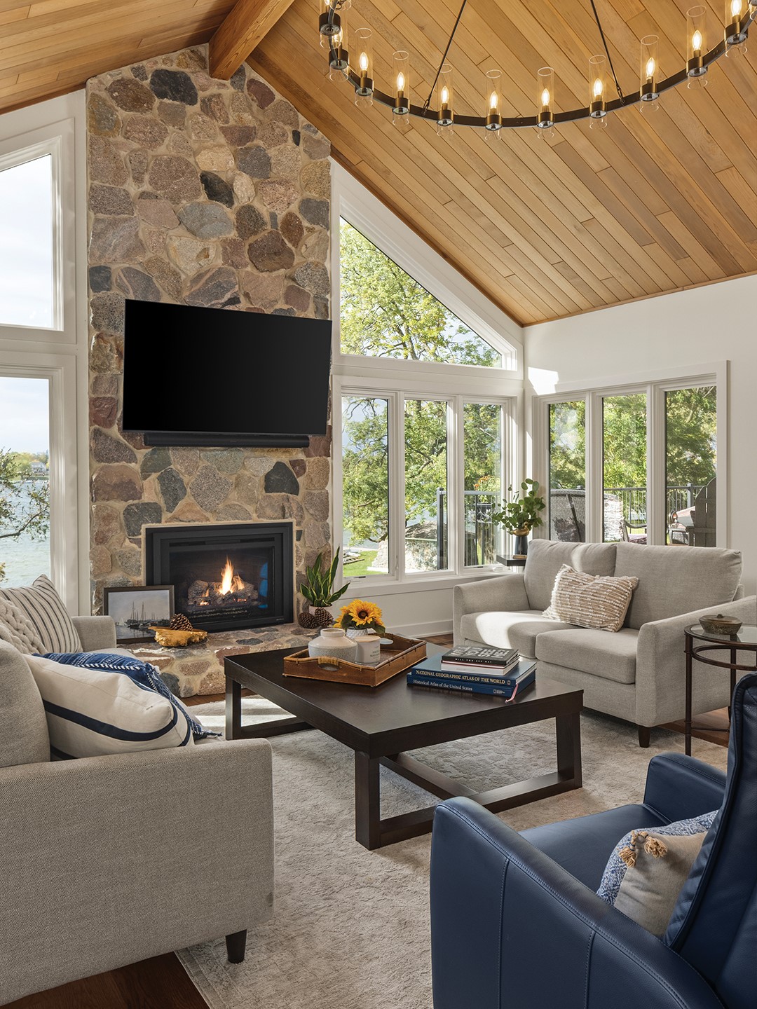 The living area preserves the original wood-planked ceiling and stone fireplace, maintaining an appreciative connection to the past. The sunken layout anchors the space for intimate family gatherings, while high-contrast elements, like warm wood flooring and deep blue seating, provide a textured, lived-in feel, explains Kimberly Fletcher, lead designer at Boyer Building Corporation. For the stairwell, the dated brass and glass railing was replaced with custom woodwork and slender black iron spindles, prioritizing transparency and light, she explains. Paired with a dramatic cascading globe fixture and grand vaulted proportions, the space feels both nostalgic and intentionally designed for a contemporary lifestyle.