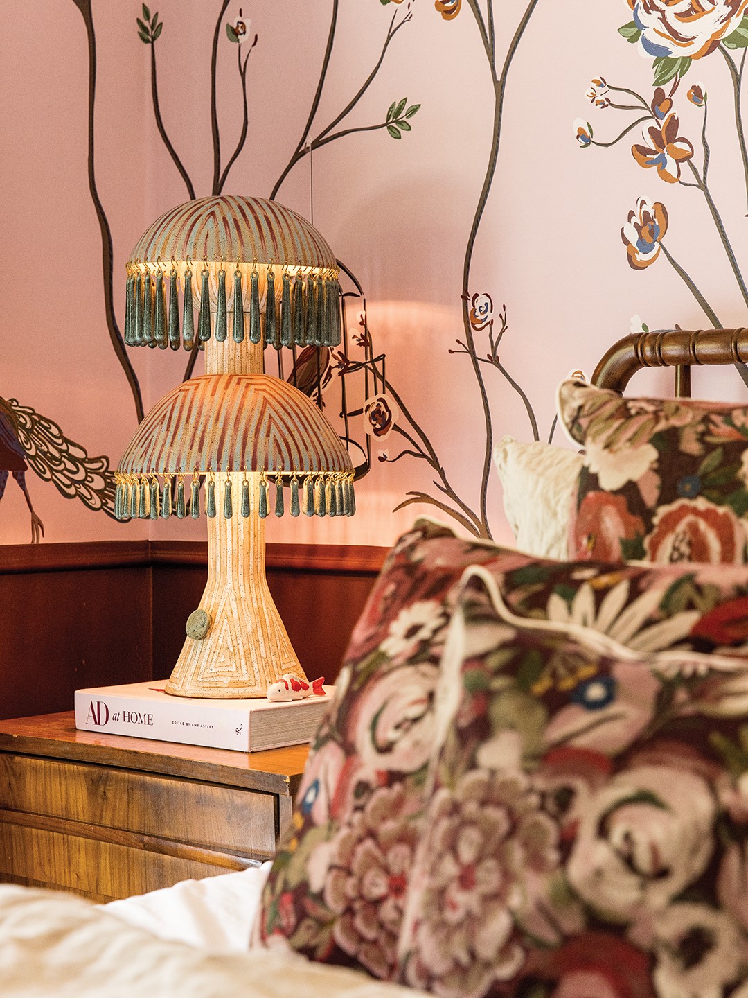 This bedroom is awash in wallpaper and pillows by She She, a stoneware glaze lamp by Jeremy Anderson and ample style to create a welcoming sanctuary. 