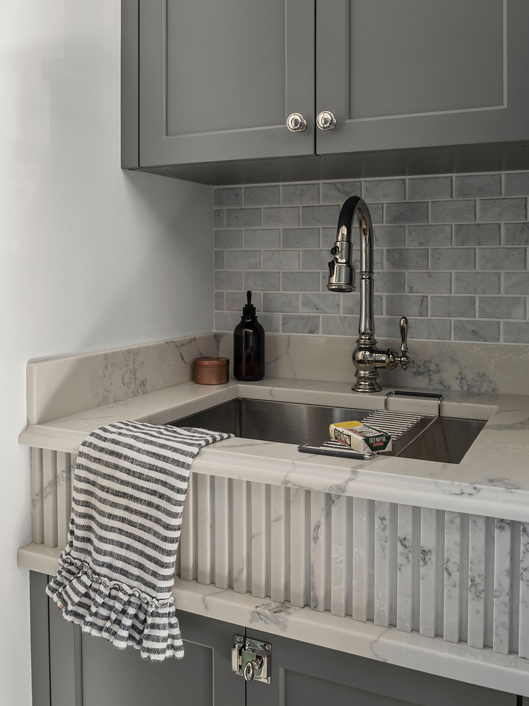 A combined mudroom and laundry space can be a recipe for clutter, but the Gormans intentionally designed against that by reducing countertop real estate that can serve as drop zones. New cabinetry extends down to meet the counterspace, thus keeping the collection zone at a minimum. Even the laundry sink received a glow up, using quartz with an Ogee edge and fluted front detail.