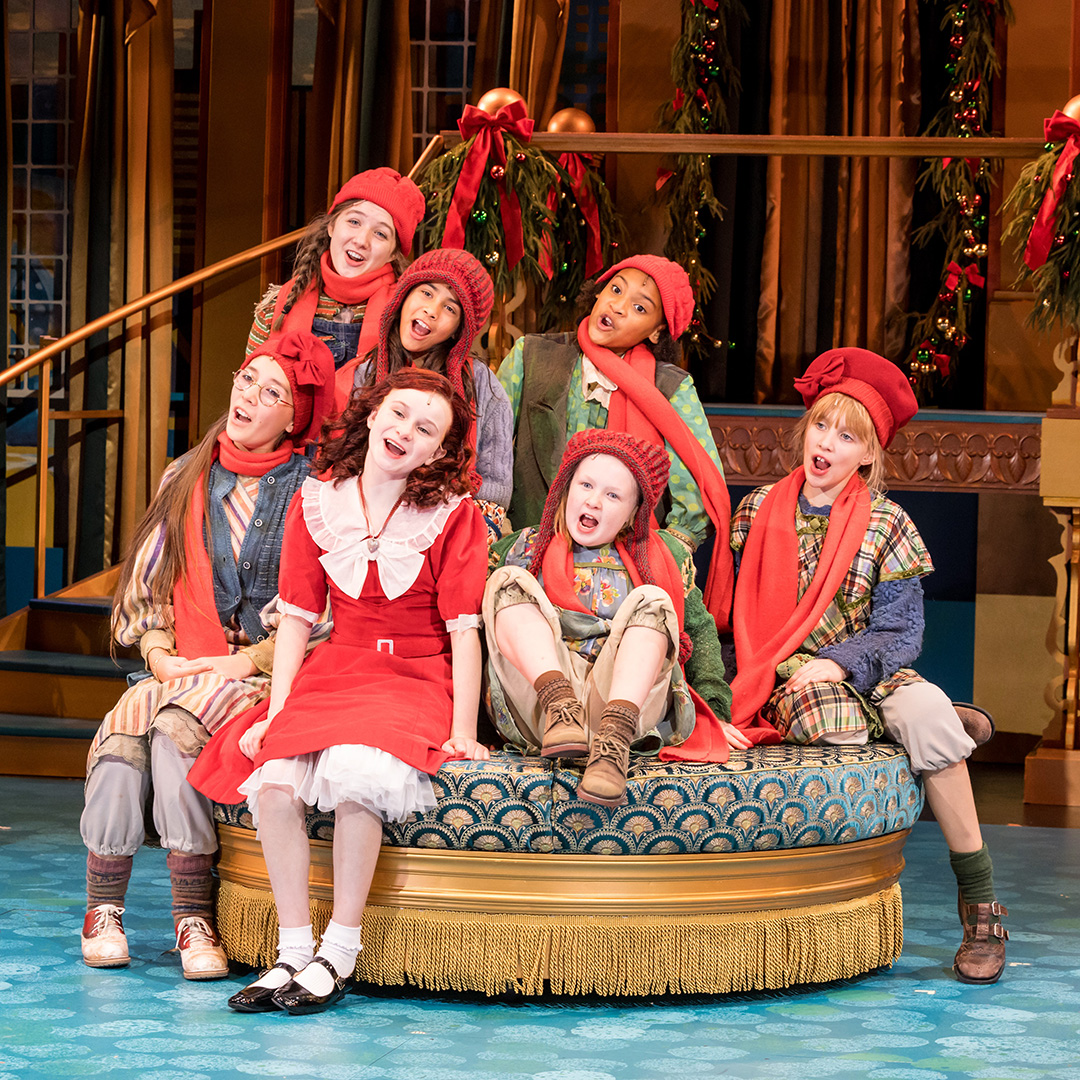 Penelope Talatinick (front left) as July sitting next to Eve Scharback (red dress) playing Annie in Chanhassen Dinner Theatres’ production of Annie.